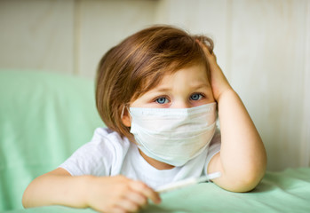 a little girl, wearing a medical mask, plays at home, in home quarantine, during the coronavirus pandemic,COVID-2019