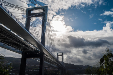 Suspension bridge with sun behind clouds