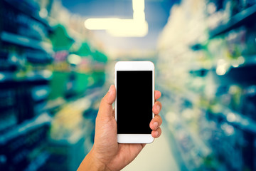 Hand hold blank smartphone on blur supermarket background