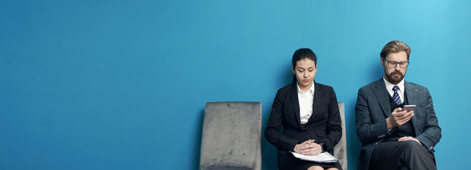 Two male and female business people waiting in line to be called into job interview at office