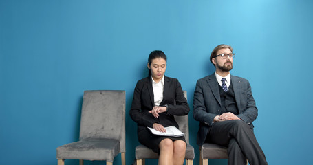 Two businesspeople sitting in queue waiting their turn for job interview, isolated blue background