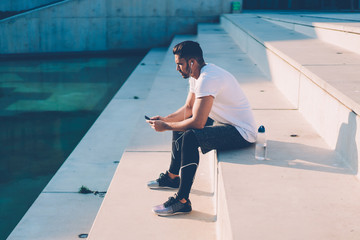 Calm sportsman surfing mobile relaxing after run in street