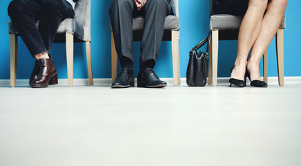 Low section of three job candidates sitting on chairs in corridor waiting for intake meeting
