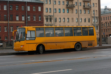 Fototapeta na wymiar yellow bus for transporting children, parked on the canal embankment on the background of old houses