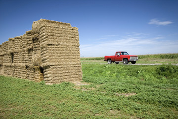 Old red pickup truck driving past hay bails on Lincoln Highway, US 30, Nebraska Byway, America's...