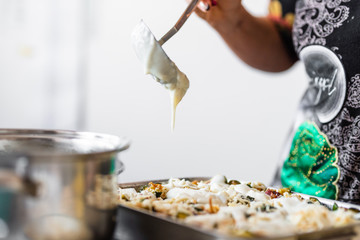 Homemade preparation of lasagna with zucchini and bacon. Close up of female hand putting and spreading bechamel and courgettes cut into small pieces on lasagna. Selective focus.Pots, plates and trays