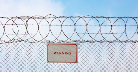 Warning sign hangs on a metal barbed wire fence