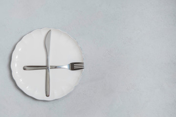 Fasting and diet concept. Empty white plate with fork and knife on neutral concrete kitchen table. Top view with copy space