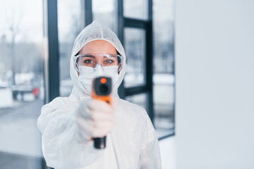 Holds infrared thermometer. Portrait of female doctor scientist in lab coat, defensive eyewear and...
