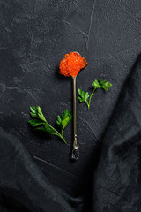 Red caviar in an exquisite spoon. Black background. Top view. Copy space