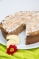 apple tart with whipped cream and cinnamon, on a plate. springlike green fabric and red primula blossom
