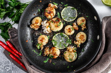 Mini grilled squid with lime and spices in a pan. Gray background. Top view