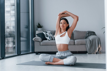 Obraz premium Does yoga exercises. Young woman with slim body shape in sportswear have fitness day indoors at home