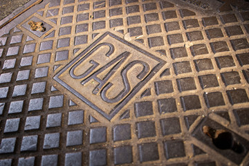 A gas manhole cover on an asphalt road in the city. Close up. Detail of iron manhole cover with sunlight reflection. Rome, Italy.