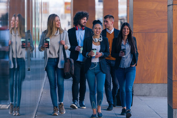 Fototapeta premium Full length of a group of colleagues in casual businesswear discussing business while walking at office hall.