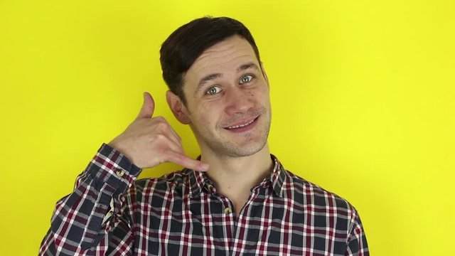A funny, cute guy asks for a callback and makes a hand gesture. Portrait of a young guy, he makes a hand gesture next to his ear asking for a callback. Portrait on a yellow background.