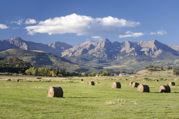 Haystacks and green grass in front of San Juan Mountains, off Route 62, Colorado, on way to...