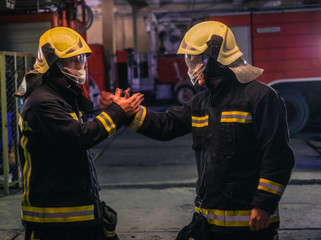 Fototapeta premium Portrait of two young firemen in uniform standing inside the fire station .