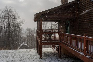 The side entrance to a brown, wooden house on the side of a mountain in the middle of a winter snowstorm.