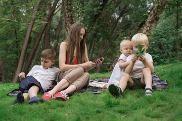 Naklejka na ściany i meble Picnic with whole family - mom and three children sitting on picnic blanket. Big happy family