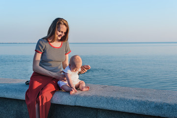 Fototapeta na wymiar Young beautiful mother and little baby on promenade on sea background.