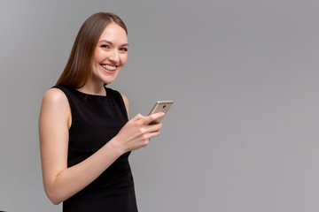 Naklejka premium Joyful emotive young european womanwith braces, holding smartphone and smiling cheerfully at camera while retelling interesting article to friend