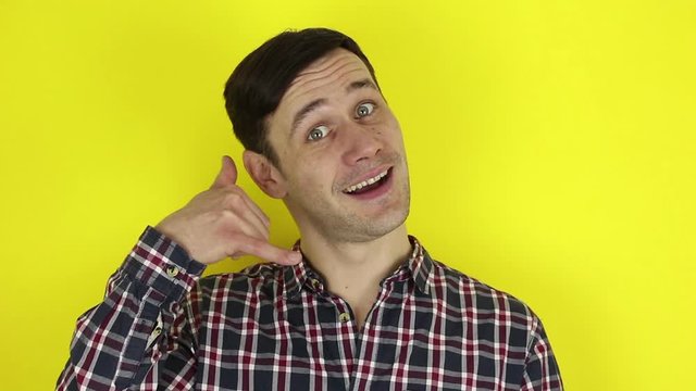 A funny, cute guy asks for a callback and makes a hand gesture. Portrait of a young guy, he makes a hand gesture next to his ear asking for a callback. Portrait on a yellow background.