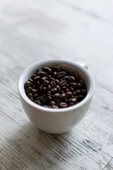 Coffee cup with coffee beans on white wooden table