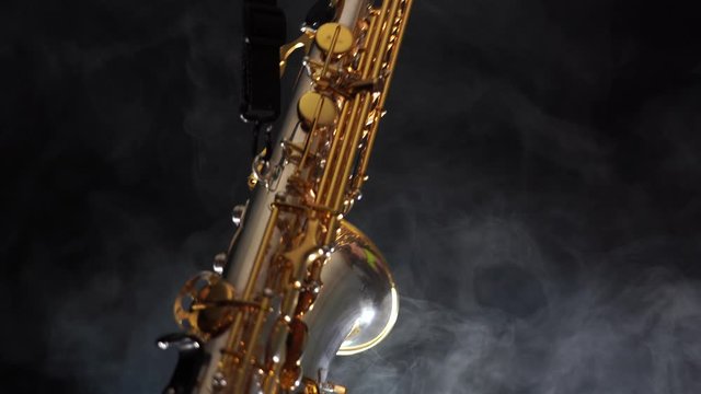 Golden shiny alto saxophone slowly move on black background with smoke