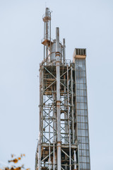 Fototapeta na wymiar A vertical view from of a tall contemporary oil refinery tower building or a fuel factory facility in an industrial zone, with plenty of pipes, metal beams, and stairs; lift shaft on the right
