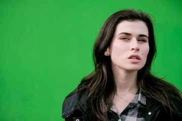 Young caucasian girl with brown hair posing on green wall.