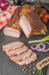 Smoked piece of meat with bacon sliced on black slate with spices. Meat dish - Pidcherevyna side view