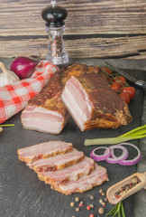 Smoked piece of meat with bacon sliced on black slate with spices. Meat dish - Pidcherevyna side view