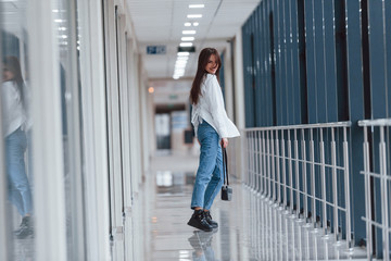 Brunette in white shirt walks indoors in modern airport or hallway at daytime