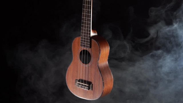 Red wood Hawaii ukulele guitar isolated against black background with smoke