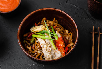 Chinese dishes in a clay plate on a black concrete background with ingredients for delivery
