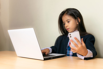 Colombian girl sitting at the desk in the classroom is doing homework on the computer and checks the cell phone