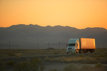 18-wheeler semi-trucks at sunset hit the highway driving down Interstate Highway 15 between Los...
