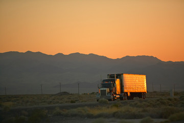 18-wheeler semi-trucks at sunset hit the highway driving down Interstate Highway 15 between Los...