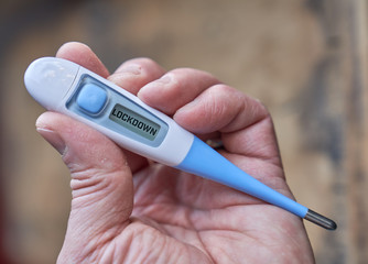 Male hand holds clinical thermometer with lockdown text on the screen during global covid-19 or corona pandemic