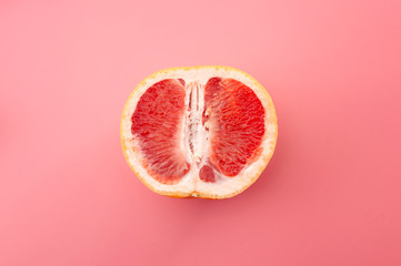 Sexuality, erotic tension and metaphor for female sexual organs concept with grapefruit isolated on pink background - obrazy, fototapety, plakaty