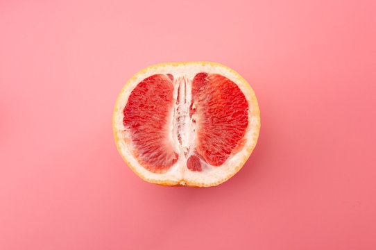 Sexuality, erotic tension and metaphor for female sexual organs concept with grapefruit isolated on pink background