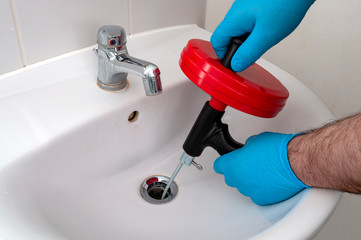 Plumbing issues, occupation in sanitation and handyman contractor concept with plumber repairing drain with plumbers snake (steel spiral that twists through pipes to collect dirt) in residential sink - 332038777