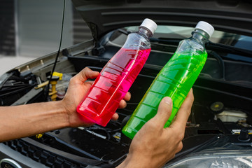 Topic of car repair shop: hands holding two products showing choice of pink or green coolant or antifreeze for cars. maintenance fluids or engine products.