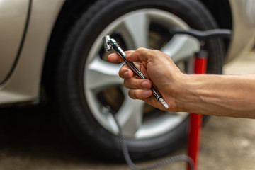 Topic of problems with the car on the road. hand holding tire gauge with manual inflation pump in the background. roadside assistance concept