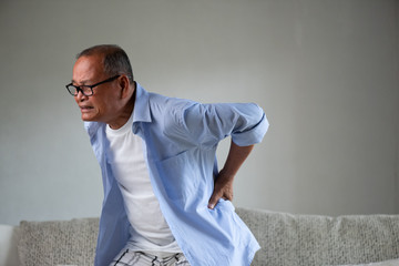 Asian old man sitting on sofa and having a back pain, backache at home. Senior healthcare concept.