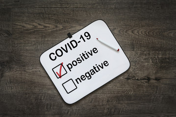 White board with positive test results for COVID-19 on a dark wooden background