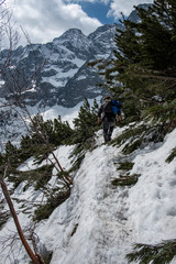 A lonely hiker in the mountains heading snow-capped peaks in the early spring