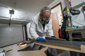 Specialist worker making carbon part with goggles, gloves and dust protection, for racing car in...