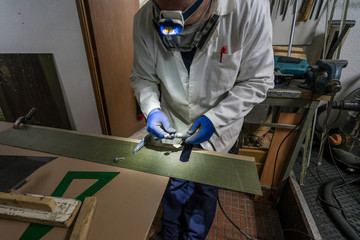 Specialist worker making carbon part with goggles, gloves and dust protection, for racing car in workshop. Preparing tool.